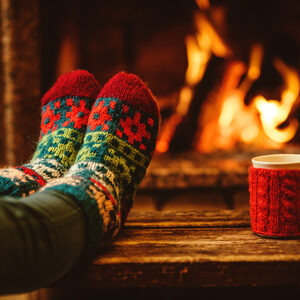 46927059 - feet in woollen socks by the christmas fireplace. woman relaxes by warm fire with a cup of hot drink and warming up her feet in woollen socks. close up on feet. winter and christmas holidays concept.
